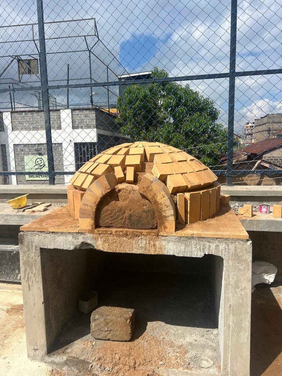 Brick pizza oven under construction on a concrete base at the Smiling Centre
